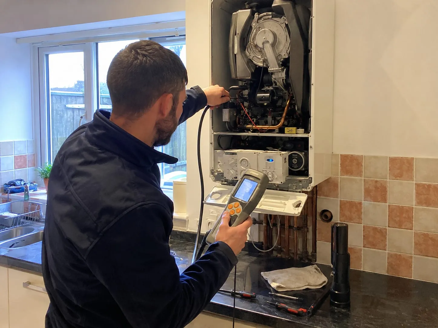 A Warmside engineer servicing a wall-mounted gas boiler, flue-gas analyser reading on show.
